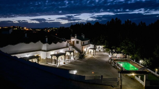 A well-lit courtyard with a swimming pool, a staircase leading to a building, and a view of the surrounding landscape.