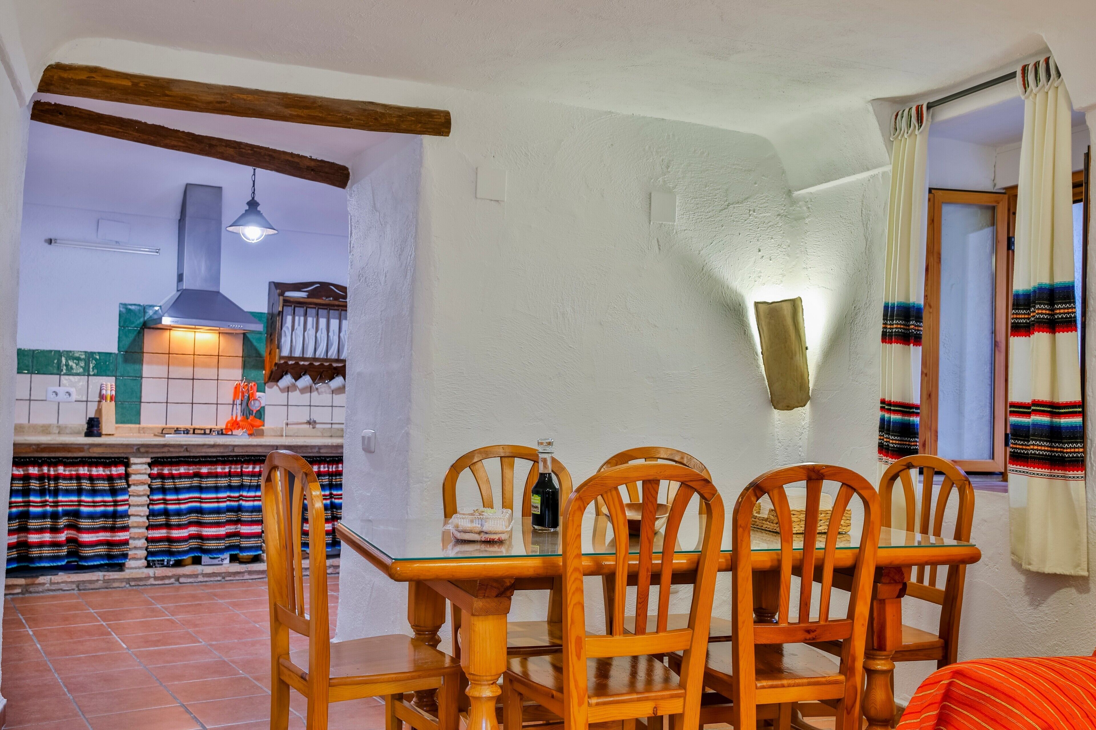 Un comedor con sillas de madera, una mesa de vidrio y una cocina al fondo.