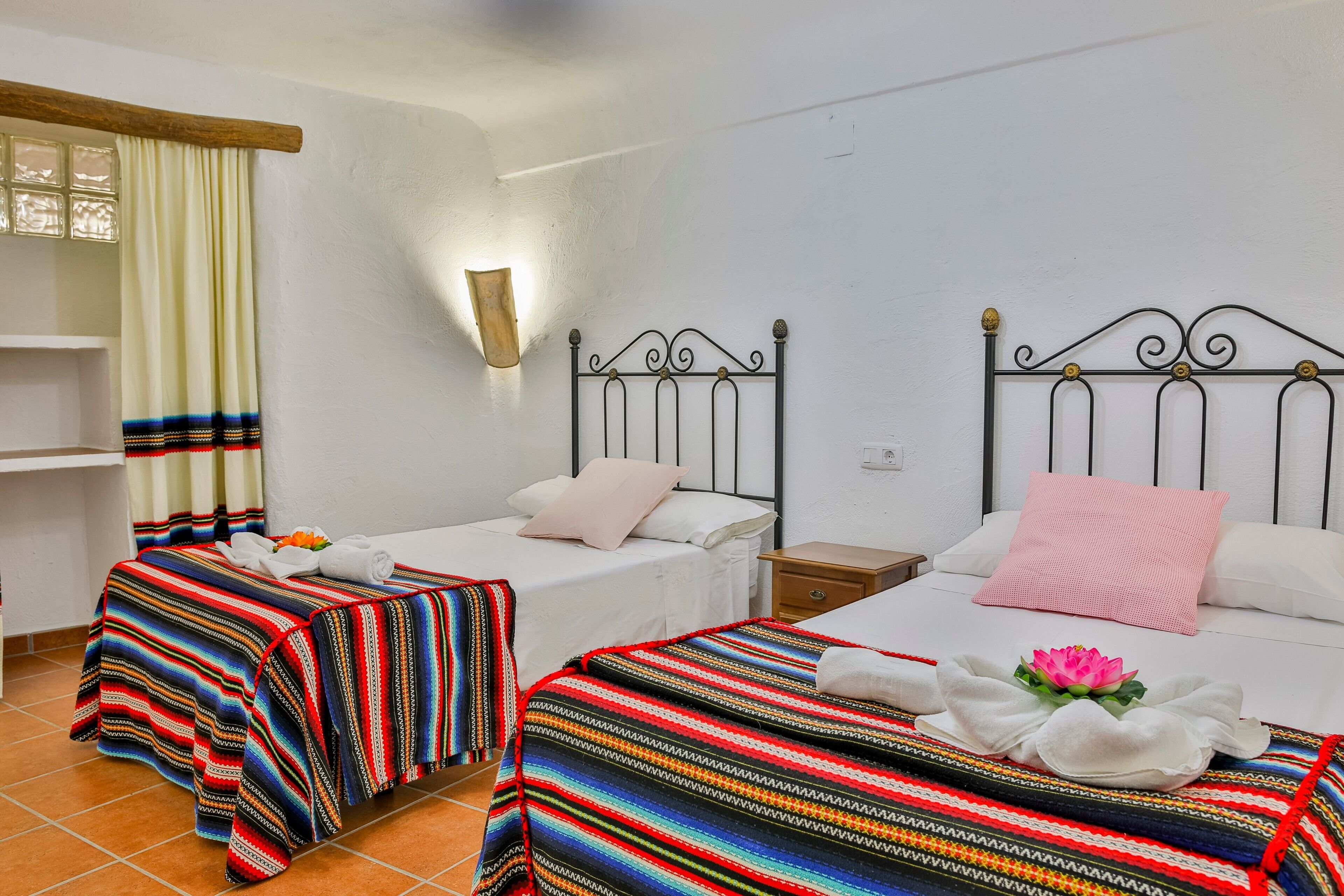 A hotel room with two beds, a nightstand, a wall-mounted lamp, and a window with curtains.