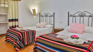 A hotel room with two beds, a nightstand, a wall-mounted lamp, and a window with curtains.
