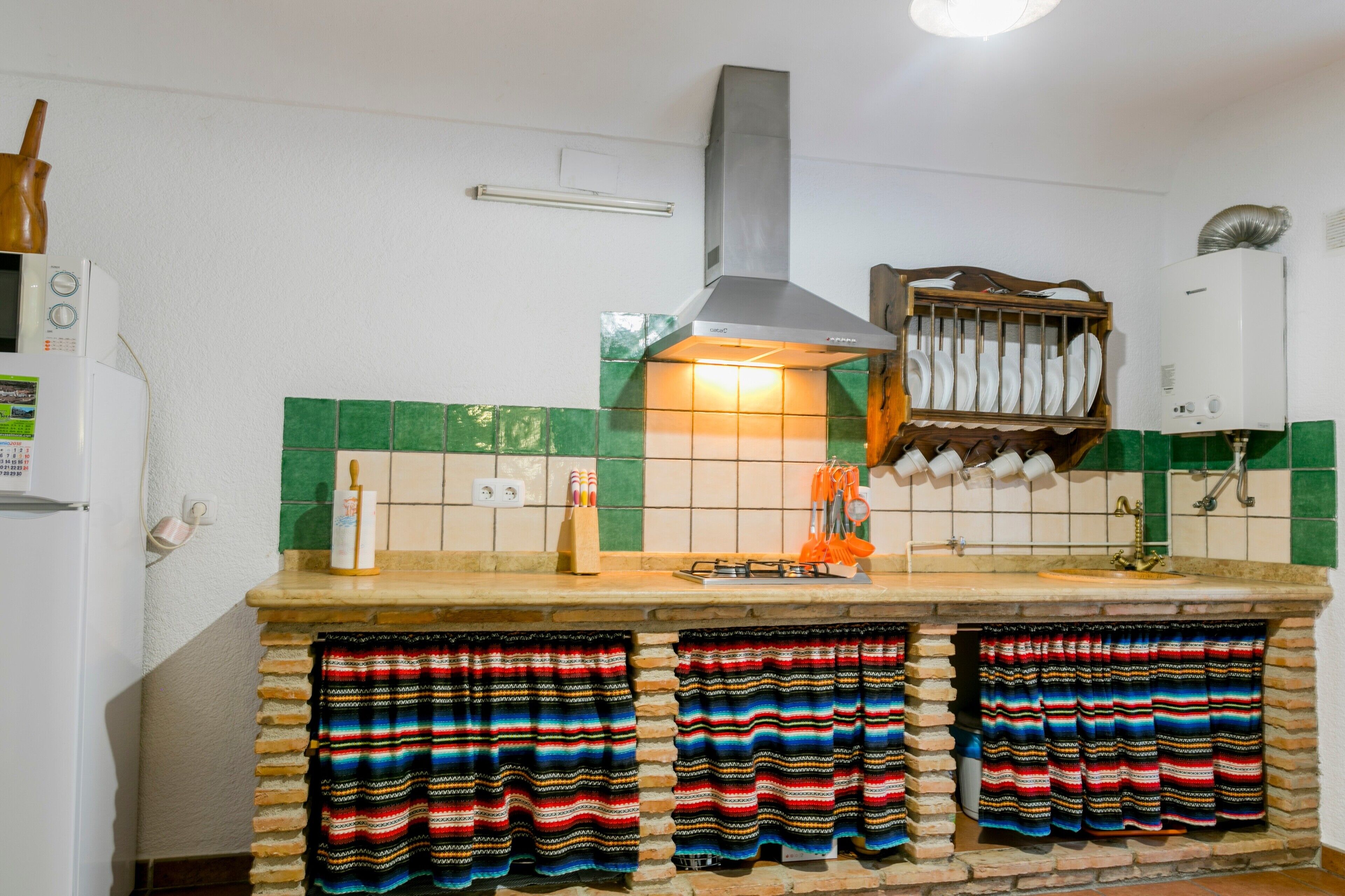 Een keuken met een kookplaat, magnetron en een rek met servies.