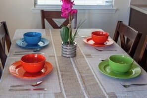 A dining table with four bowls and spoons, a potted plant, and chairs around it. - Room C, >30 days, Near Medical Center, WOMEN ONLY (Houston)