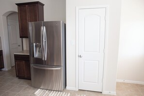 Un refrigerador de acero inoxidable, gabinetes de madera, una puerta blanca y piso de baldosas color beige en una cocina.