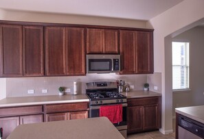 A kitchen with wooden cabinets, a stainless steel microwave, a gas stove, and a dishwasher. - Room C, >30 days, Near Medical Center, WOMEN ONLY (Houston)