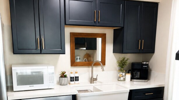 Una cucina moderna con mobili scuri, un piano di lavoro bianco, un lavello, un forno a microonde, una macchina per il caffè e una ciotola di limoni su un vassoio di legno.