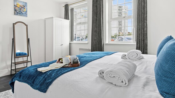 A hotel room with a bed, a mirror, a window with curtains, and a painting on the wall.