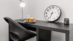 A desk with a clock, a lamp, a plate with food, and a candle.