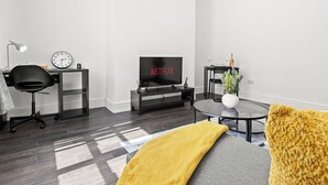 A modern living room with a TV, a desk, a chair, a round coffee table, and a sofa.