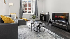 A modern living room with a sofa, coffee table, TV, and a window with curtains.