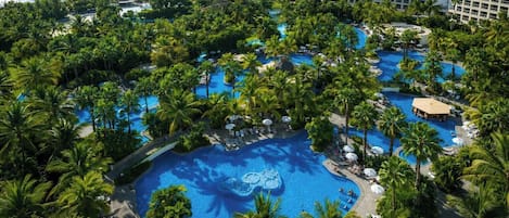 A resort with multiple swimming pools surrounded by palm trees and a beachfront view.