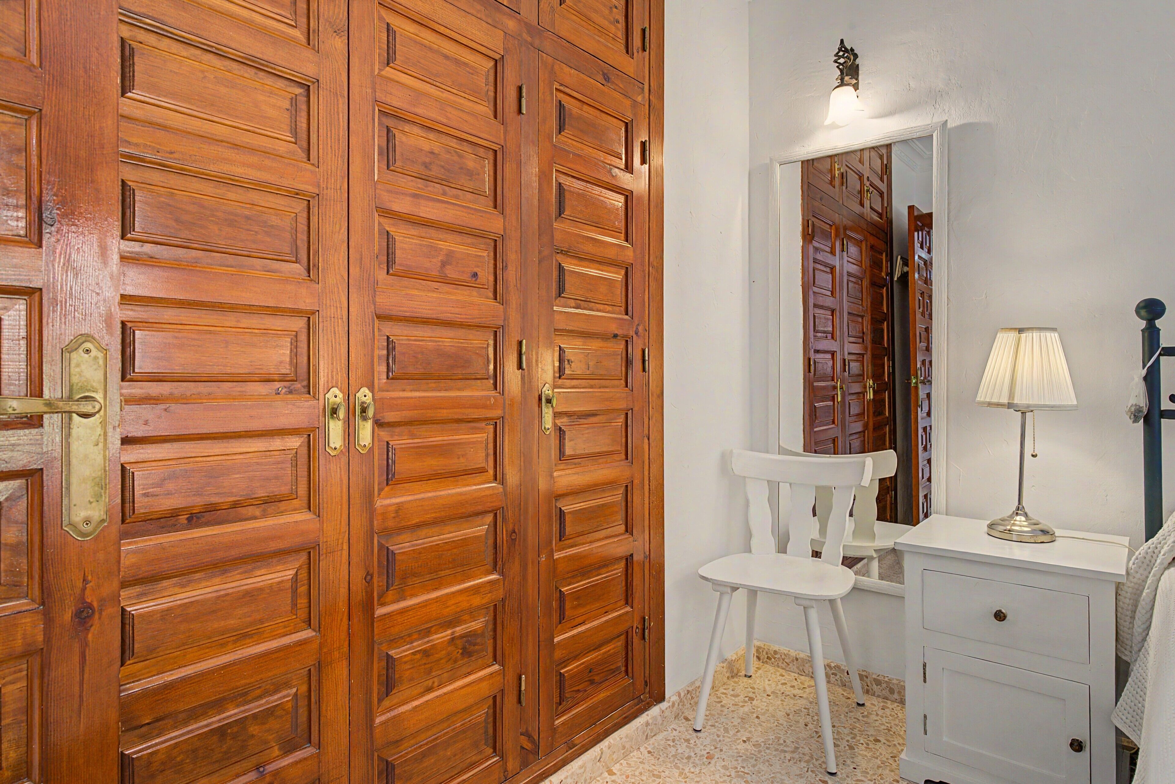 Une pièce comprenant une armoire en bois, une chaise blanche, une petite table et un miroir.