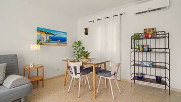 Een ruime, goed verlichte kamer met een eettafel, stoelen, een bank, een lamp, een schilderij, een potplant en een boekenkast.