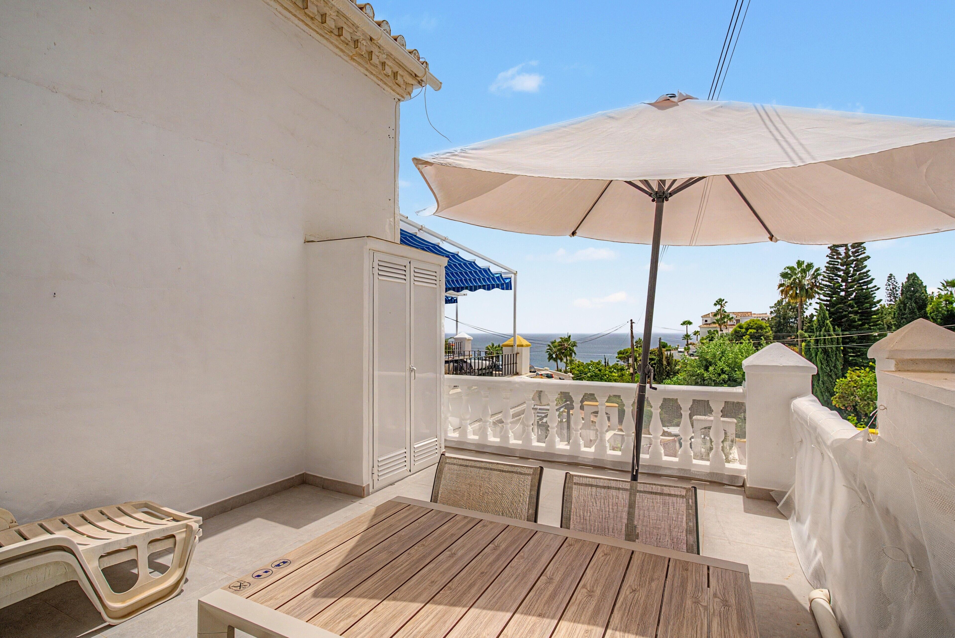 Un balcon avec une table et des chaises, un parasol et une vue sur la mer.