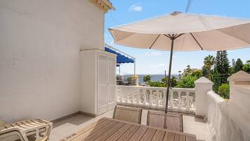 Un balcon avec une table et des chaises, un parasol et une vue sur la mer.
