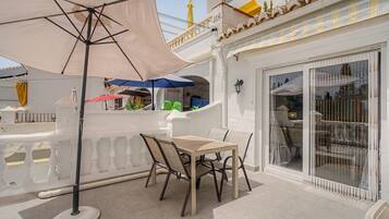 Een terras met een tafel en stoelen, een grote parasol en een gebouw met een balkon.