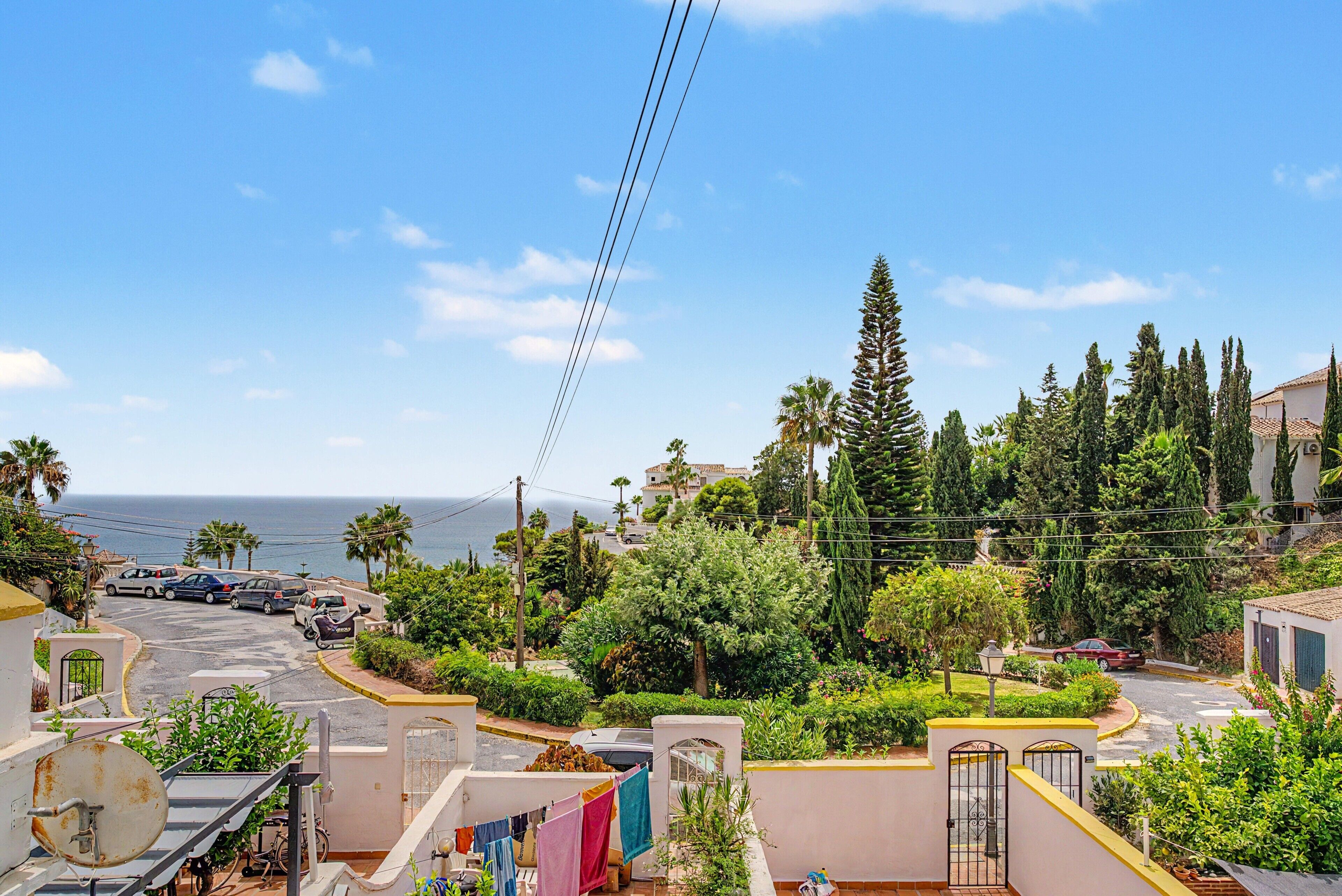 A residential area with a view of the sea, parked cars, and lush greenery.