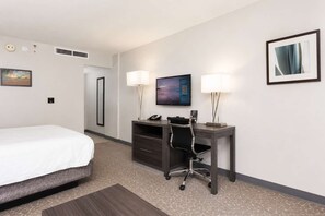 Ein Hotelzimmer mit Bett, Schreibtisch, Stuhl, zwei Lampen, einem Fernseher und einem gerahmten Bild an der Wand.