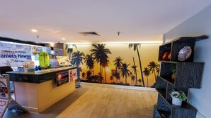 Un área de recepción con mostrador, un mural de palmeras en la pared y un cartel con información sobre excursiones y actividades.