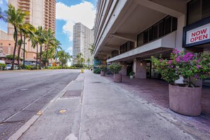A hotel with a 'NOW OPEN' sign, a sidewalk with planters, and tall buildings in the background. - The Aqua Palms | Near Waikiki Beach + Free Parking (Honolulu)
