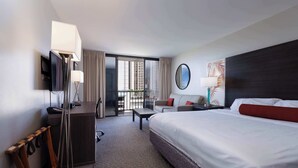 Habitación de hotel con una cama grande, un escritorio, una silla, un televisor y un balcón con cortinas.