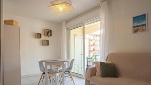 Una sala de estar con un sofá, una mesa de comedor con sillas, una lámpara colgante y un ventanal corredero que da a un espacio exterior.