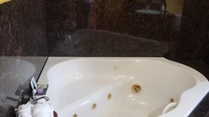 A bathroom with a white bathtub, a towel, and a dark marble countertop. - Providencia Motel (Burbank)