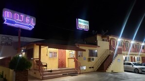 A motel with a neon sign, a staircase, and a parked car. - Providencia Motel (Burbank)