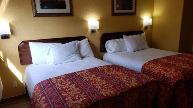 Two beds with white linens, a patterned red bedspread, and wall-mounted lamps. - Providencia Motel (Burbank)