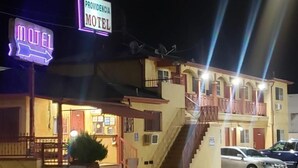 A motel with a neon sign, a staircase, and a parked car. - Providencia Motel (Burbank)