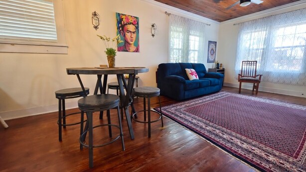 Una habitación con un sofá azul, una mesa redonda con taburetes, una alfombra estampada y obras de arte en las paredes.