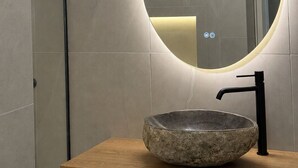 A bathroom with a round mirror, a stone basin, and a modern faucet. -   Junior Suite with Modern Design in Chania (Chania)