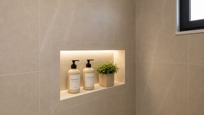 A bathroom with a shelf containing two bottles of shampoo and conditioner, and a small potted plant. -   Junior Suite with Modern Design in Chania (Chania)