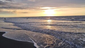 A beach with waves, a sunset, and a clear sky.