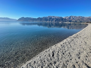 Un lago transparente con una playa de guijarros y montañas al fondo.