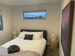 A hotel room with a bed, two bedside lamps, a window with a view of buildings, and a large painting on the wall.