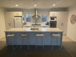 Een moderne keuken met een centraal eiland, barkrukken, een roestvrijstalen afzuigkap en een magnetron.