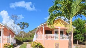 A pathway leading to two pink buildings with balconies, surrounded by greenery and palm trees. - Creole bungalow with views of the ocean and tropical scenery – Le Tapeur, Guadeloupe (Pointe-Noire)