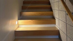 A modern staircase with wooden steps and a glass railing, leading to a landing with framed artwork. - Stunning beachside family retreat (Wellington)