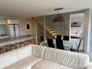 A modern living room with a sofa, dining area, staircase, and kitchen.