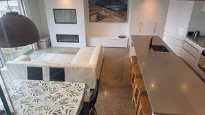 A modern kitchen with a central island, a dining area with a patterned tablecloth, and a large window with a view of the outdoors. - Stunning beachside family retreat (Wellington)
