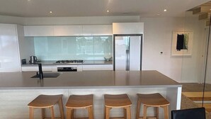 A modern kitchen with a central island, bar stools, and a dining area. - Stunning beachside family retreat (Wellington)