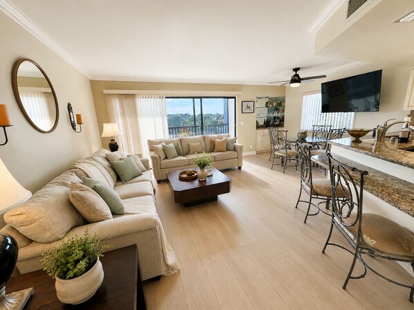 A modern living room with a sofa, coffee table, and dining area with chairs. - Serene 2-bedroom condo in charming Jupiter Ocean & Racquet Club, (Jupiter)