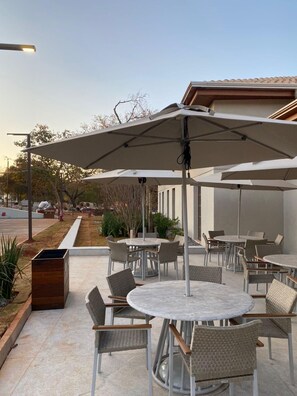 Un patio al aire libre con mesas y sillas redondas, sombrillas y un edificio al fondo.
