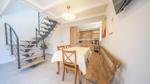 A dining area with a wooden table and chairs, a spiral staircase, and a kitchen in the background. - Maison en pierre dans un hameau privé (Pont-l'Abbé)