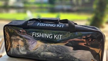 Een heldere, reflecterende visgerei tas met de tekst 'FISHING KIT' erop, geplaatst op een houten ondergrond buiten.