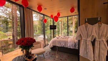 A modern bedroom with a large bed, a sitting area with a coffee table, and a view of the outdoors.