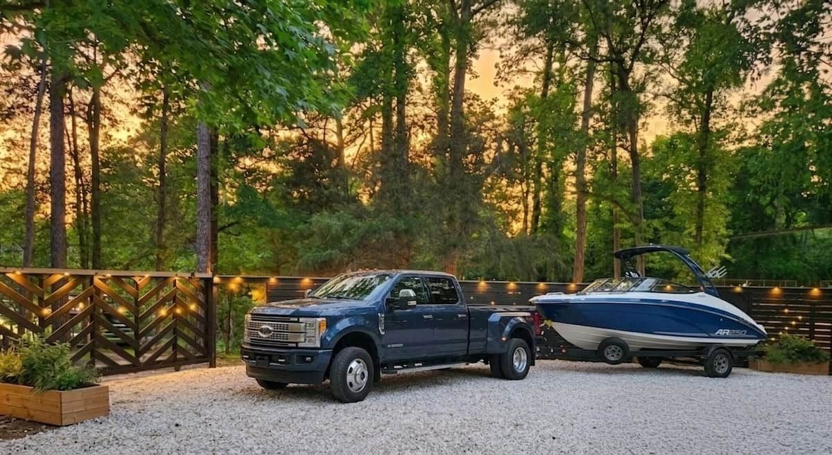 A pickup truck with a boat trailer parked on gravel.