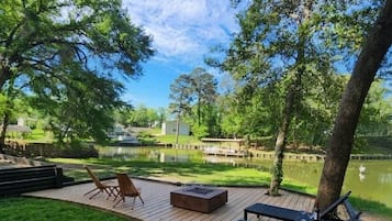 Een terras met buitenmeubilair met uitzicht op een waterpartij, omgeven door bomen.