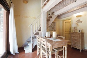 Una escalera de madera que lleva al segundo piso, una mesa de comedor con sillas, un mueble de madera y una pared con detalles decorativos.