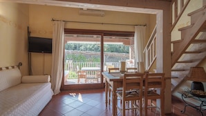 Habitació amb un sofà, una taula amb cadires, una televisió i una escala.
